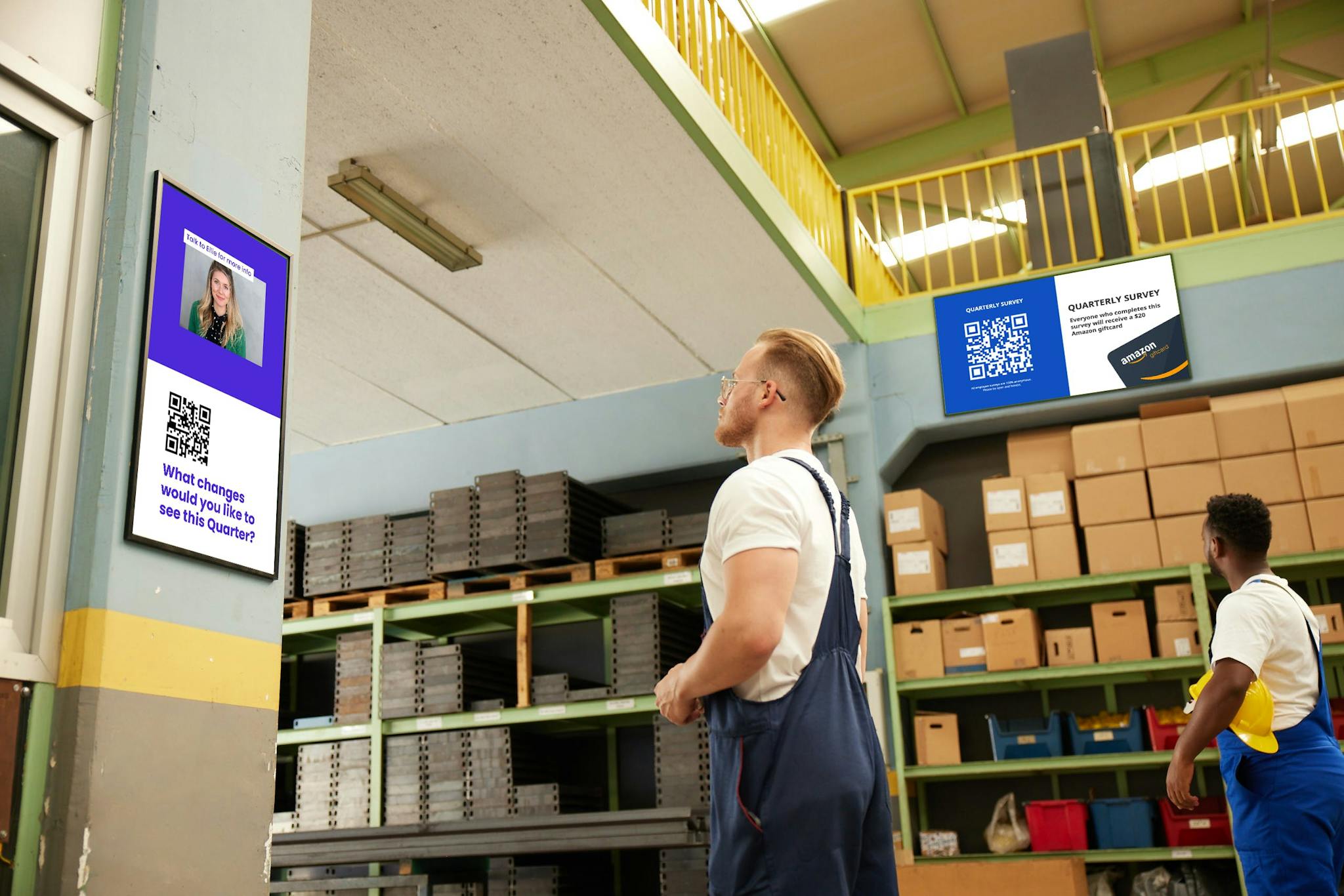 A factory floor with two screens of digital signage and two employees in front of the screens.